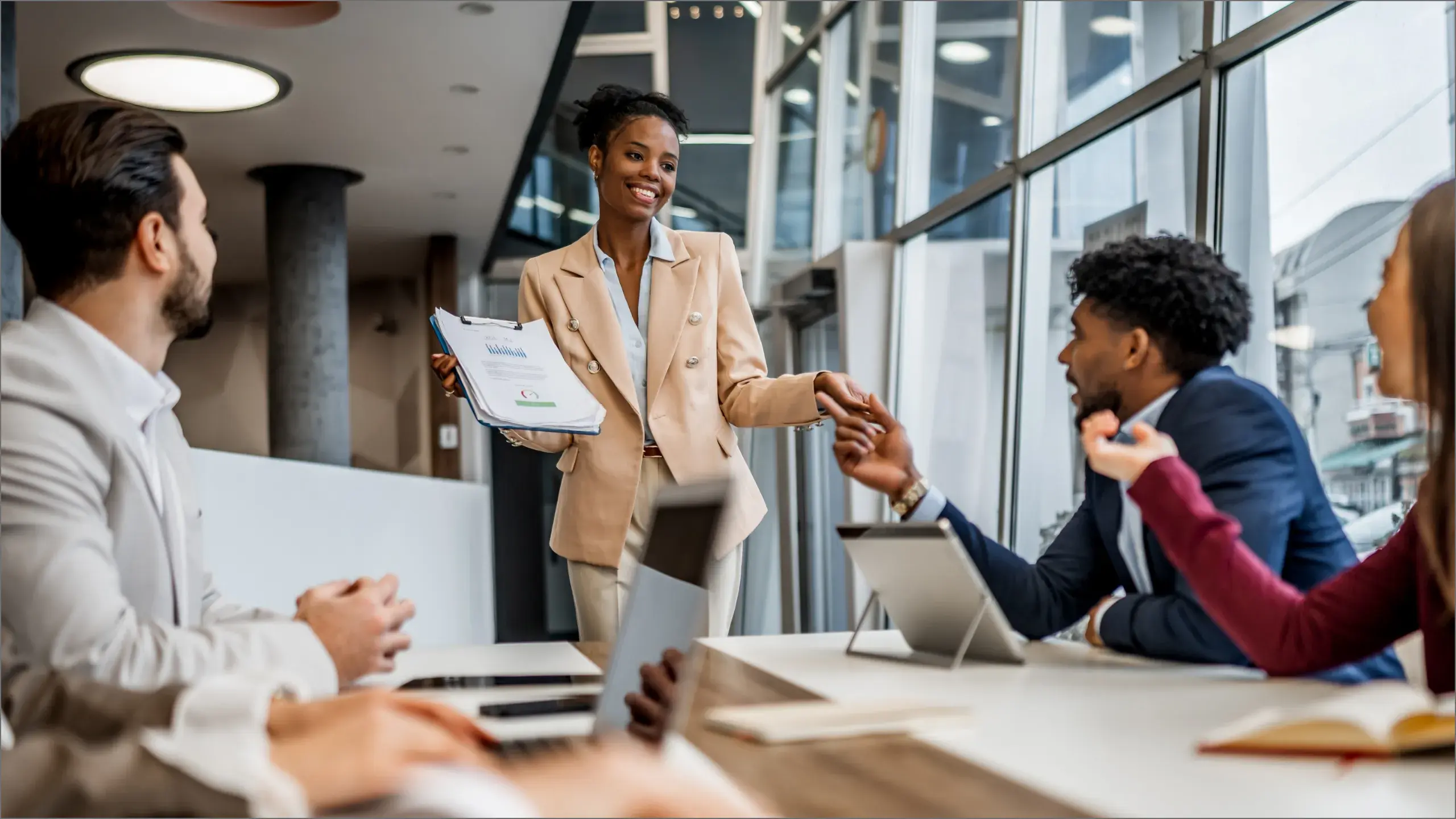 Professionals meeting around a conference table as a woman holding a document shakes a colleague's hand